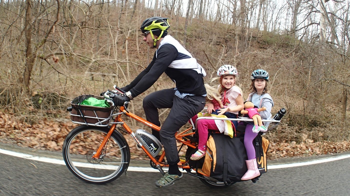 Adult carrying two kids on a longtail cargo e-bike